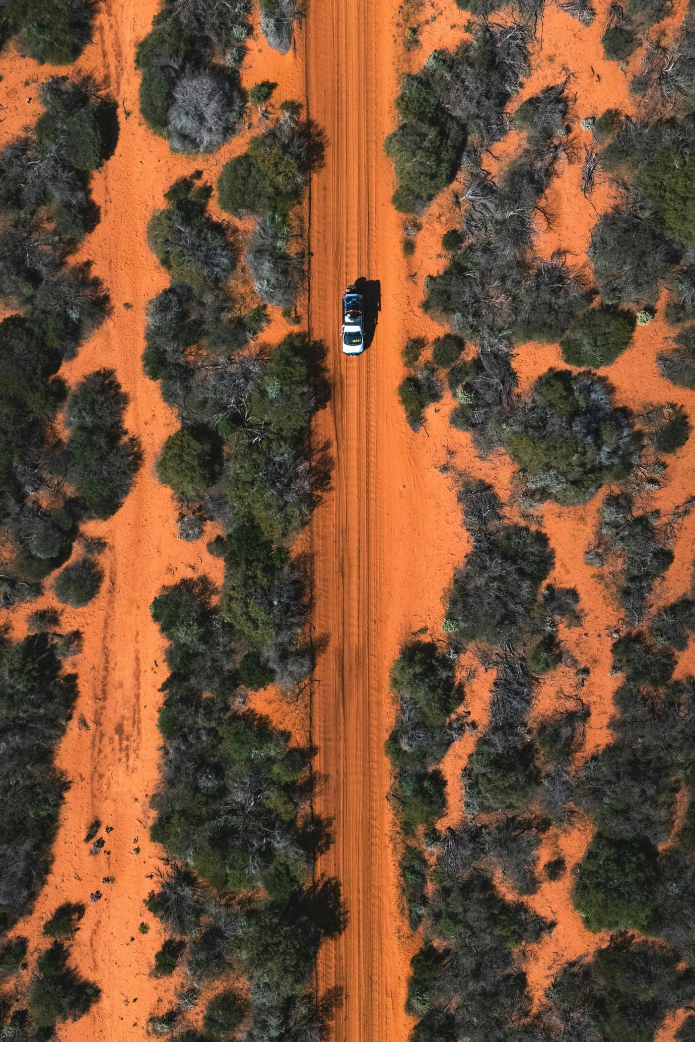 Aerial view of a vehicle on a red dirt road through scrubland